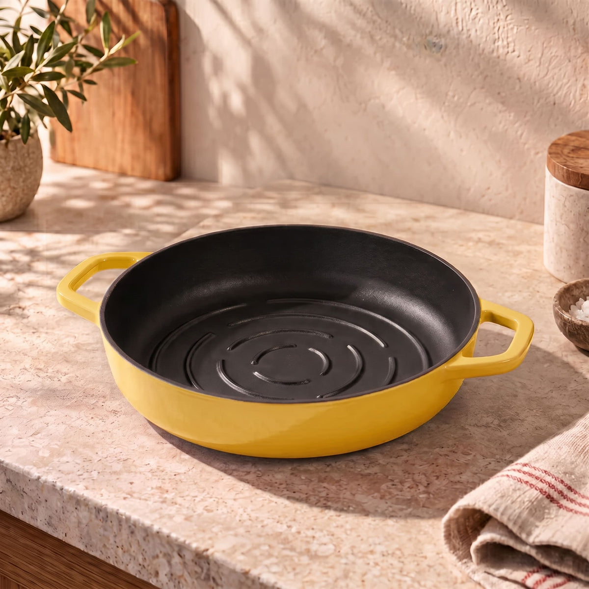 A round butter yellow cast iron bread panwith side handles sits on a beige stone countertop in a warm, sunlit kitchen setting.
