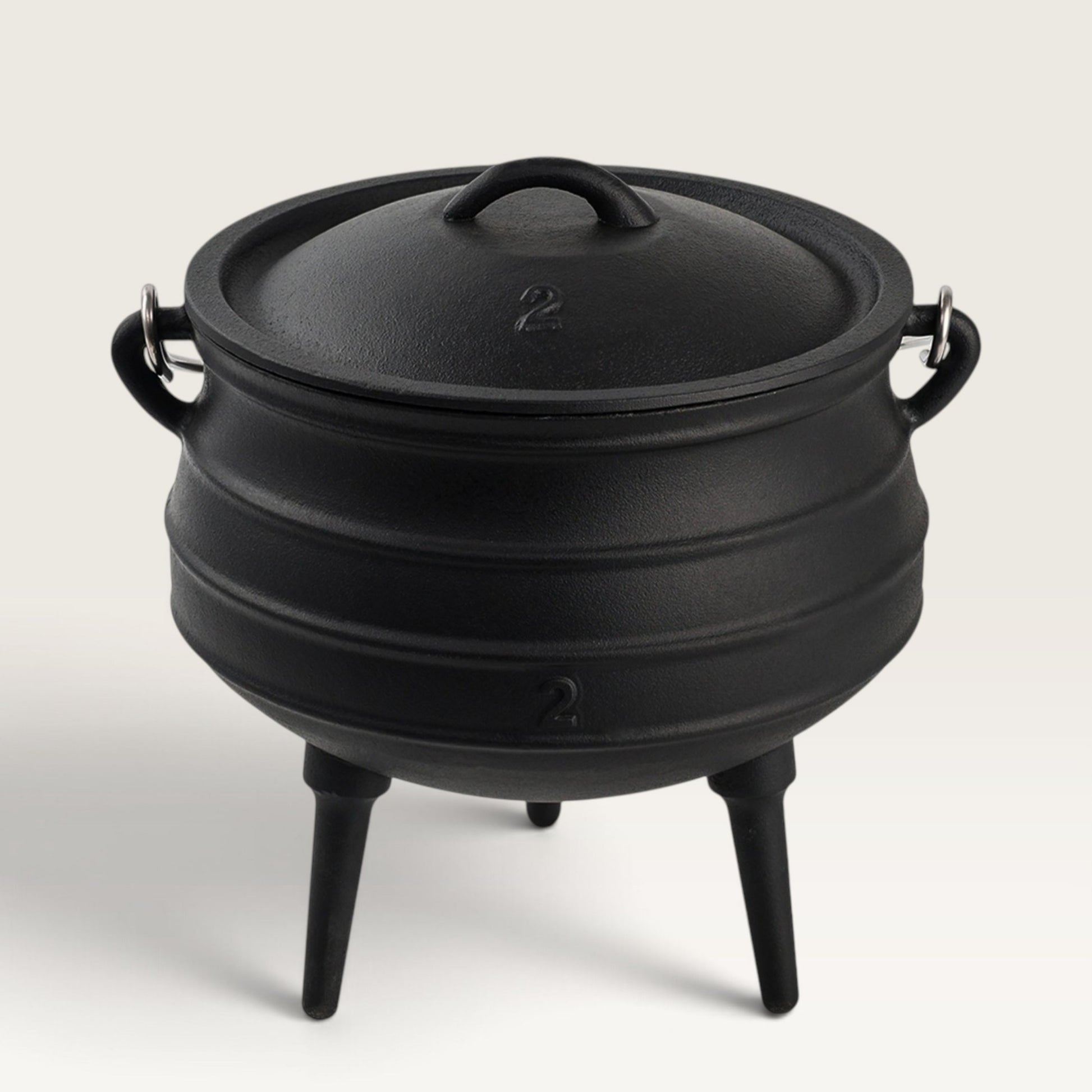 A black cast iron cauldron-style pot with a lid, side handles, and three legs, photographed on a clean light gray studio background. 6 qt Potjie