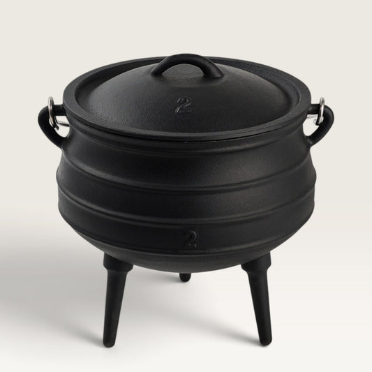 A black cast iron cauldron-style pot with a lid, side handles, and three legs, photographed on a clean light gray studio background. 6 qt Potjie
