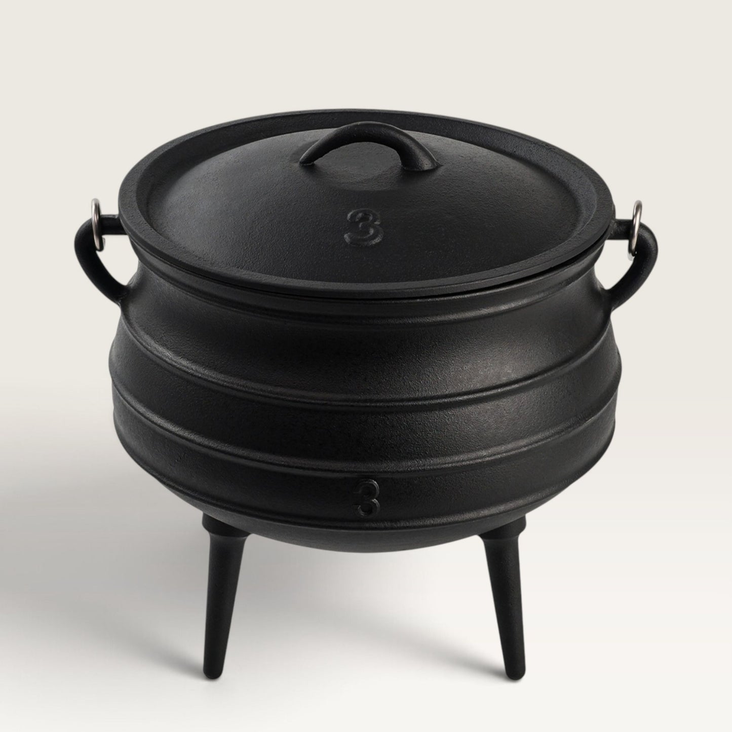 A black cast iron cauldron-style pot with a lid, side handles, and three legs, photographed on a clean light gray studio background. 8 qt potjie