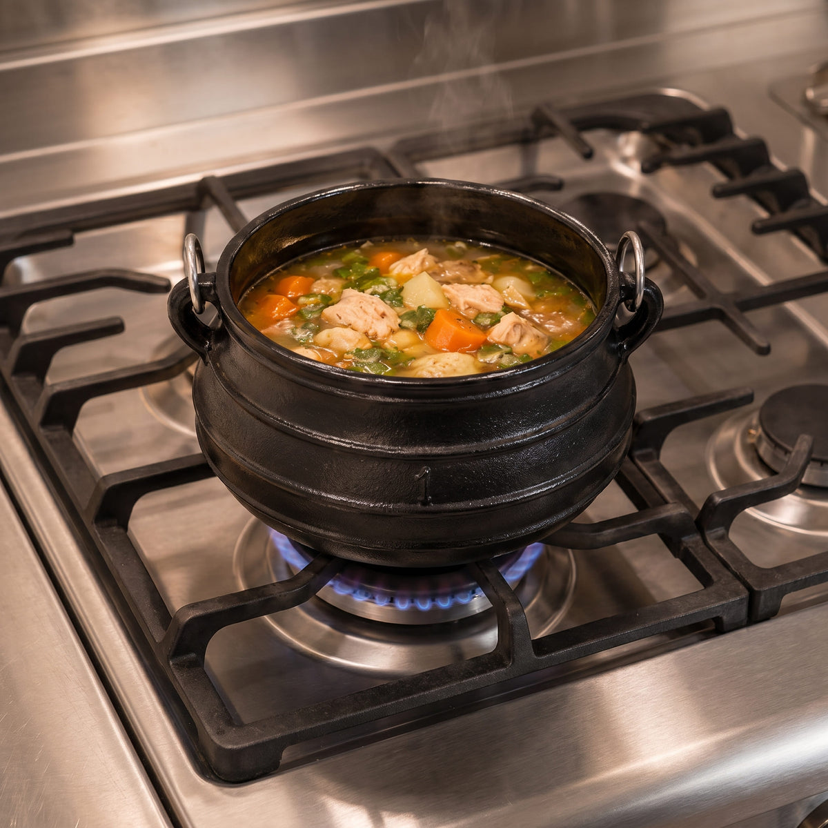 A black cast iron cauldron-style pot filled with a hearty soup or stew, simmering on a blue gas flame over a stainless steel gas stovetop. 4 qt cast iron cauldron