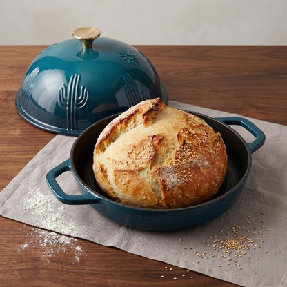Teal enamel bread oven with domed lid open, holding a round loaf in the pan.