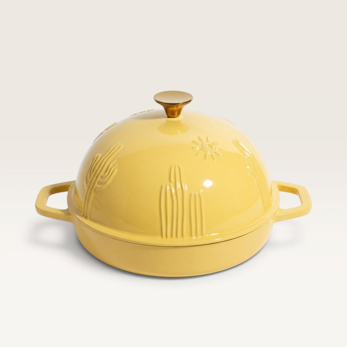 A butter yellow cast iron bread oven with a matching lid, featuring embossed cactus and sun motifs, set against a clean off-white background.