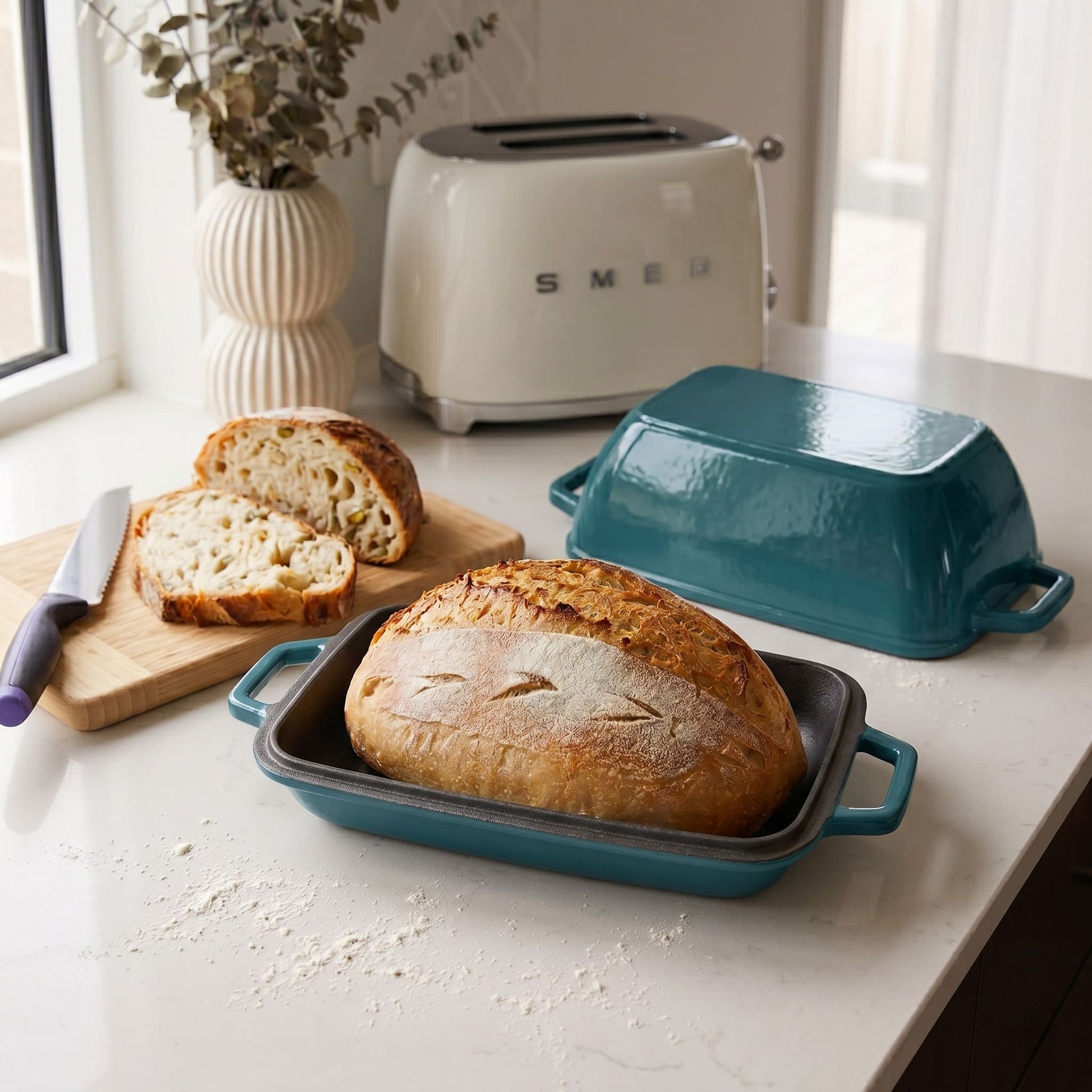Oval bread oven with baked loaf, teal base and lid on countertop