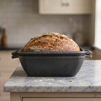 Oval bread oven with lid, bread loaf inside on countertop