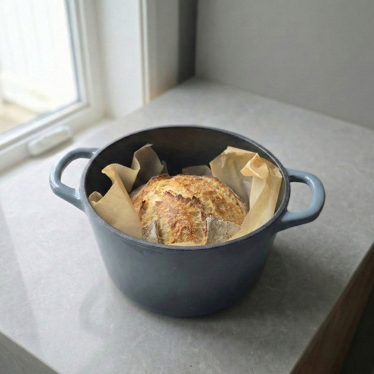 Slate blue deep Dutch oven on countertop with parchment-lined bread and side handles