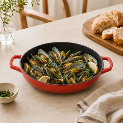 Cherry Red shallow braiser with black interior and handles, filled with mussels and lemon