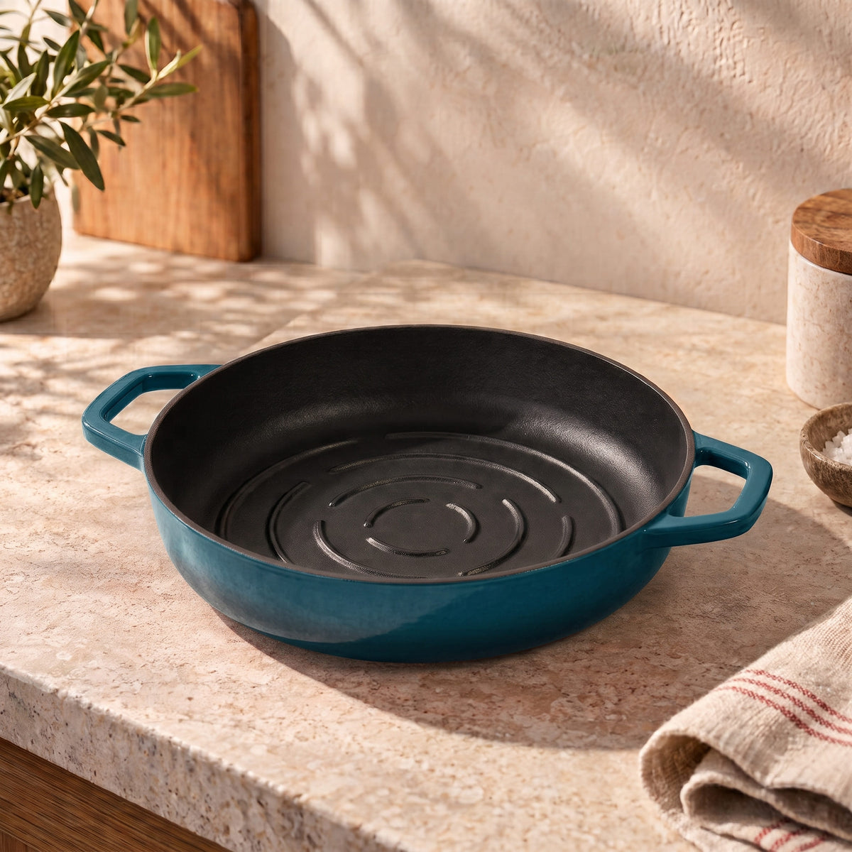A deep cyan cast iron bread pan with a black interior sits on a beige stone countertop in a warm, sunlit kitchen setting.