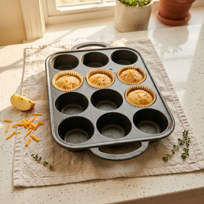 Muffin baking tray with golden mini muffins in cups on a light table.