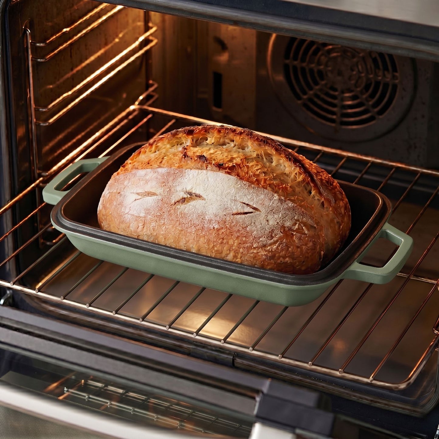 Sage green oval bread oven in an oven, with a baked loaf on the tray