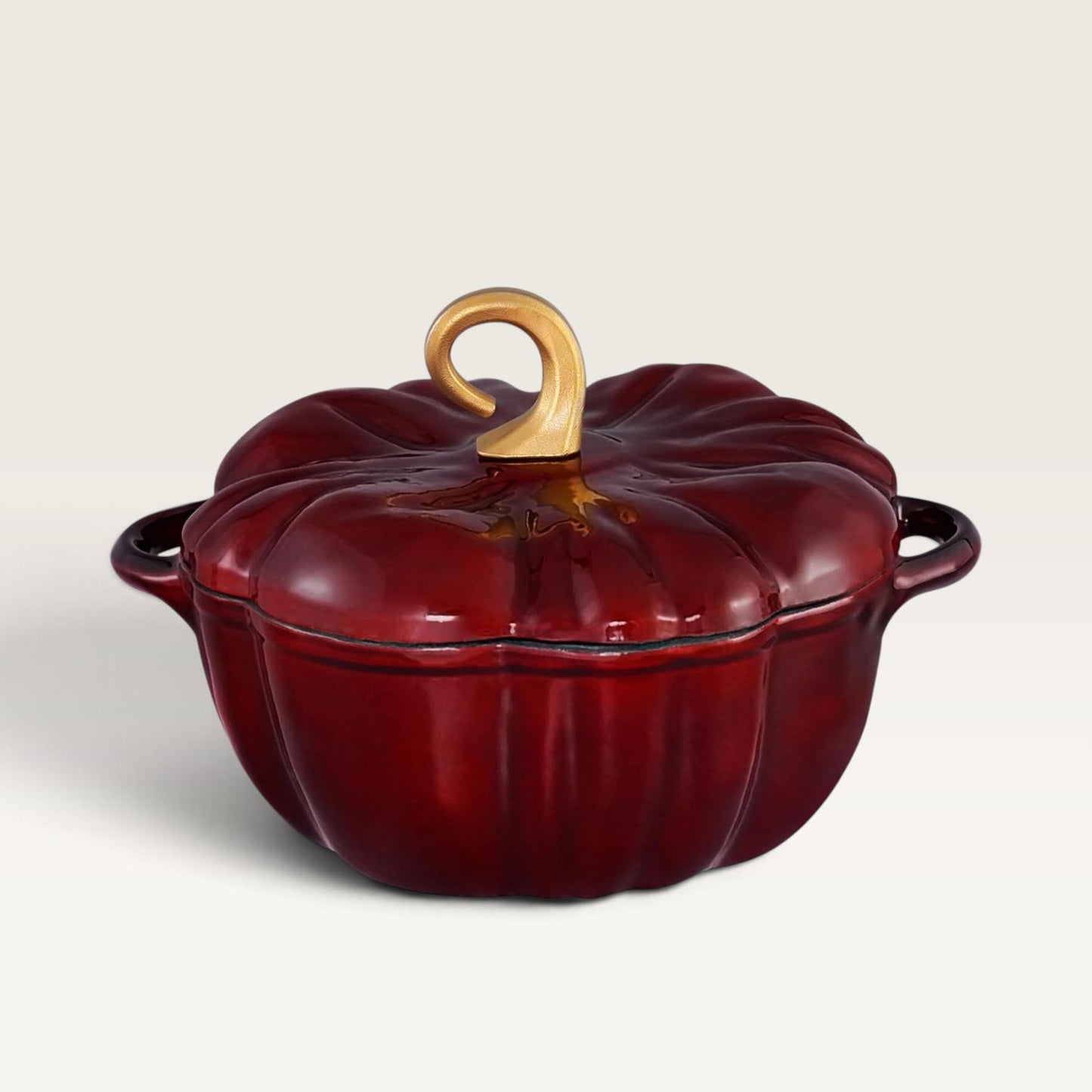 A glossy burgundy red pumpkin-shaped enameled cast iron pot with a matching lid and a light wood handle, shown on a clean off-white background.