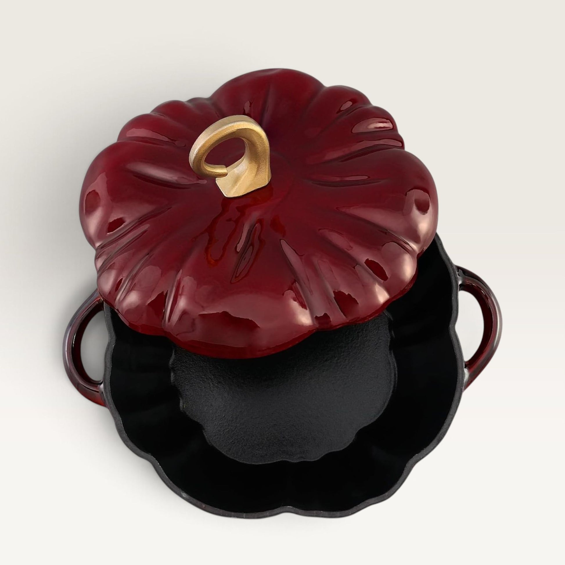 A decorative pumpkin-shaped lidded pot or casserole dish in glossy burgundy red enamel, shown with the lid partially open to reveal a black interior. The lid has a sculpted pumpkin form with a small gold handle, and the base has side handles.