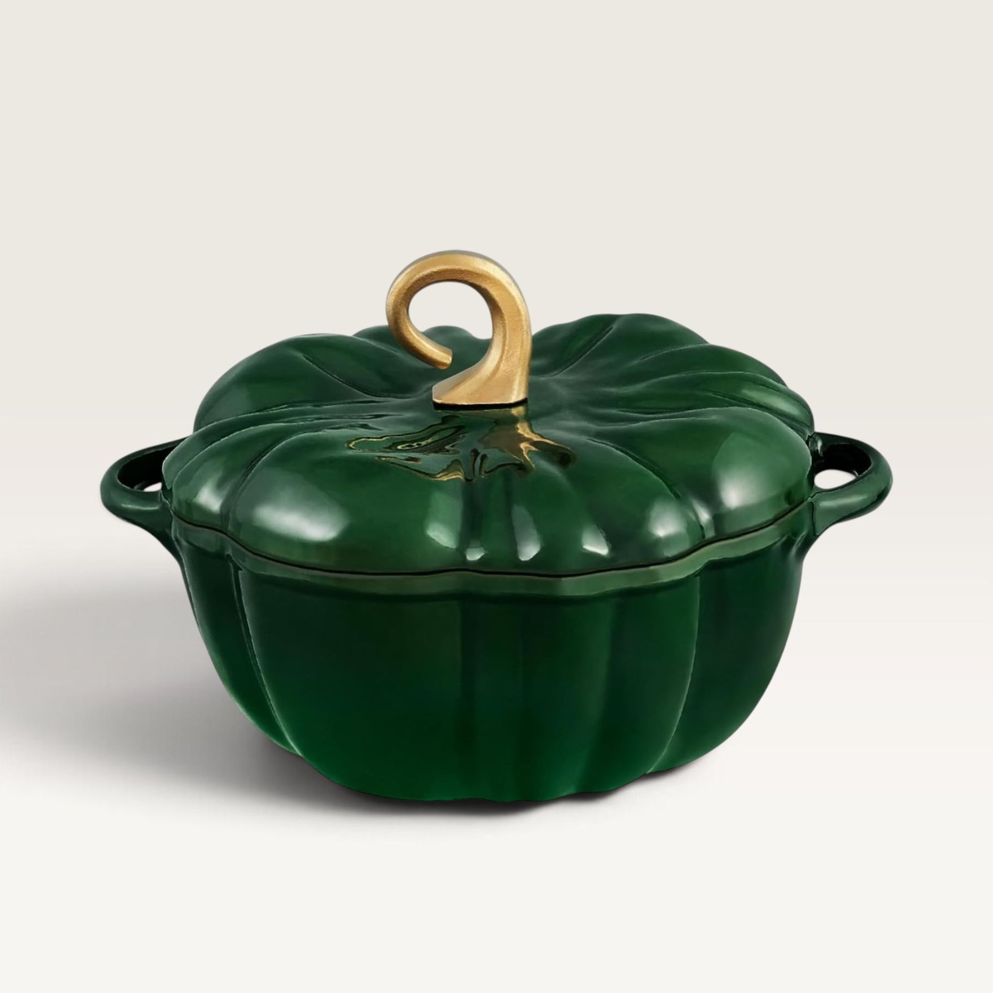 A deep green pumpkin-shaped lidded casserole pot with gold-toned handle and trim, photographed on a clean light gray studio background.