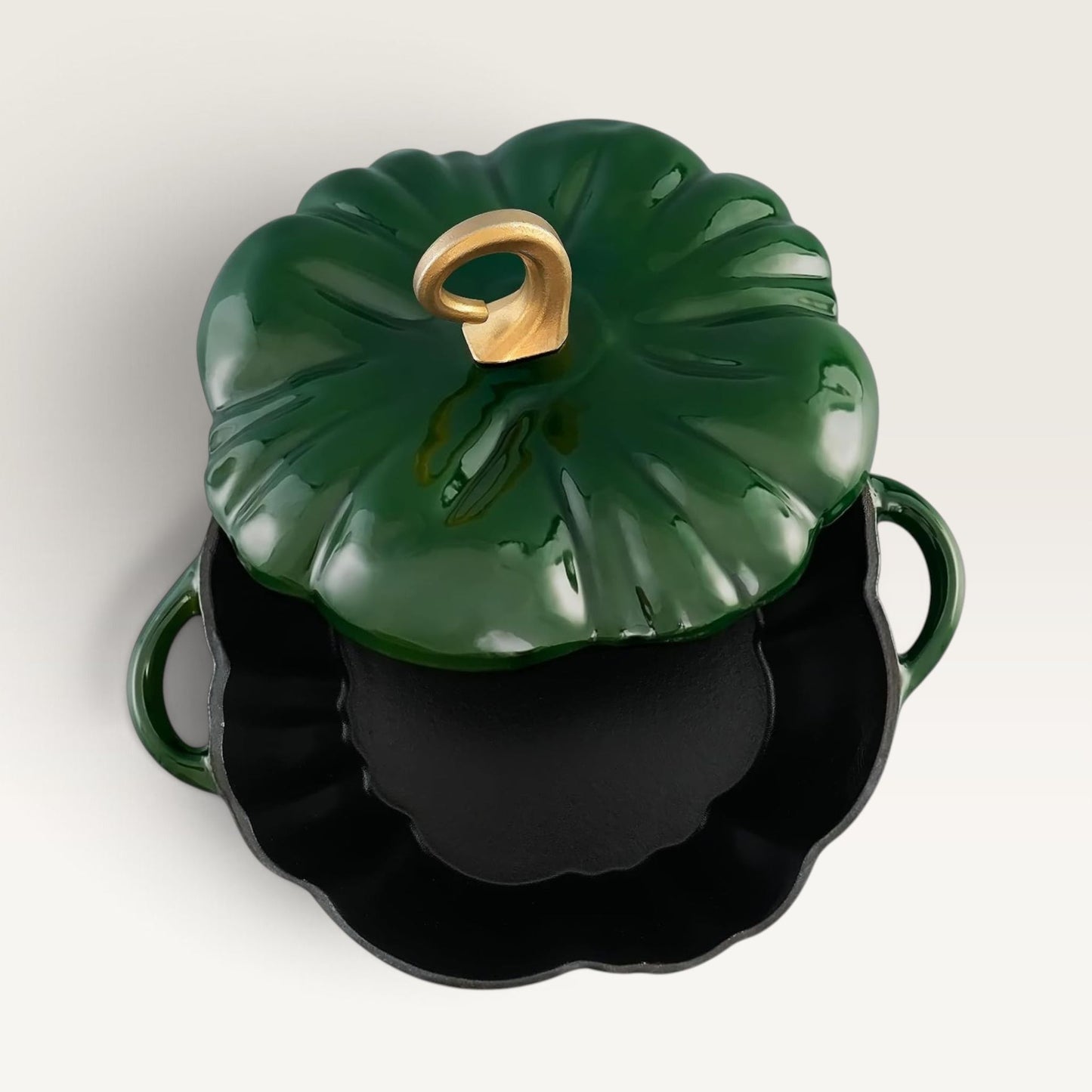 A glossy deep green pumpkin-shaped lidded pot with a gold-toned stem handle, shown open to reveal a black interior, on a clean off-white background.
