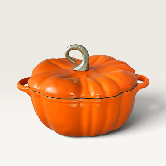 An orange pumpkin-shaped enameled cast iron Dutch oven with a matching lid and a silver metal handle, shown on a light beige background.