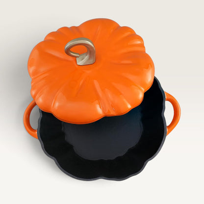 A pumpkin-shaped lidded pot with a bright orange exterior, silver handle detail on top, and a black interior, shown on a clean off-white background. 