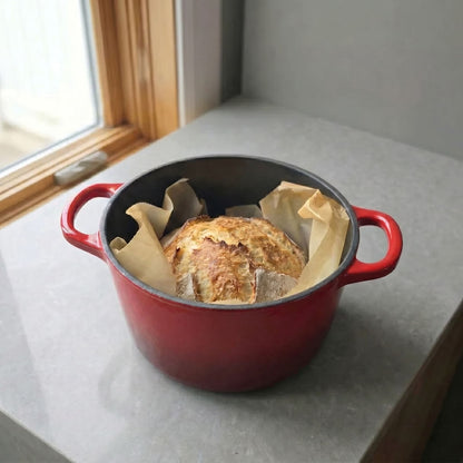 Red deep dutch oven with lid removed, holding bread wrapped in parchment